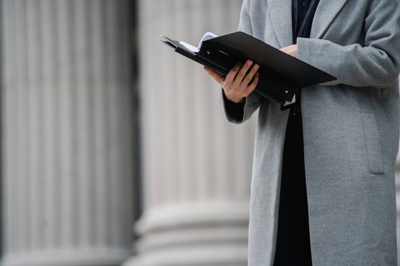 Professional woman in grey coat holding a folder of documents outside a building with columns.